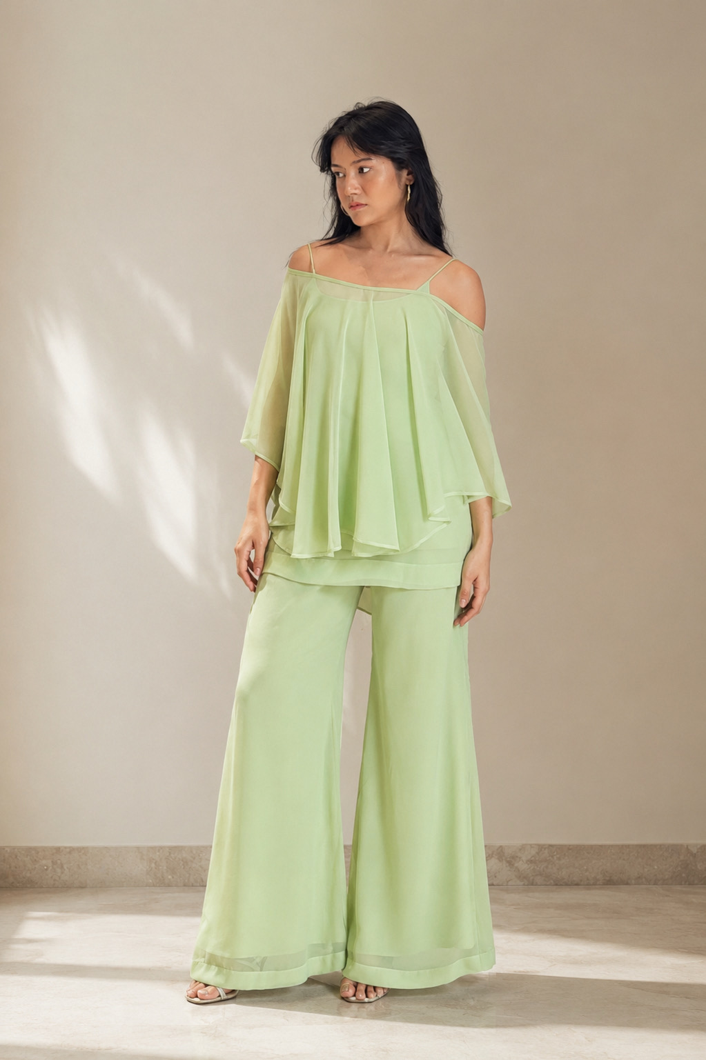 Woman wearing the Elara pistachio green georgette cape kurti set with off-shoulder cape top and wide-leg palazzo, front view